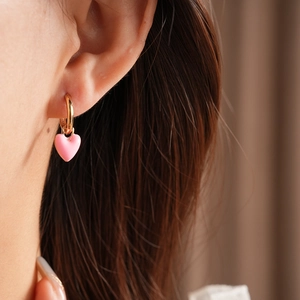 Close-up of vintage pink heart enamel earrings worn by a model in soft lighting