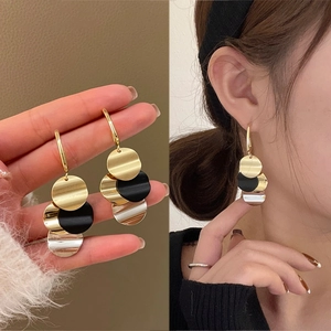 Detail view showing long geometric tassel earrings with gold black and silver metal discs