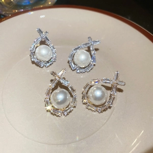 Detailed view of silver and gold pearl earrings with baguette-cut zircon in a ceramic tray