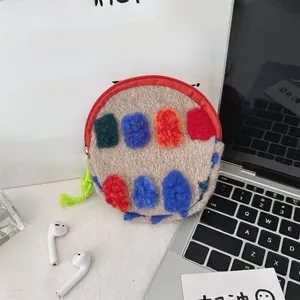 Detail of round plush pouch with colorful pom-poms, red zipper and green strap