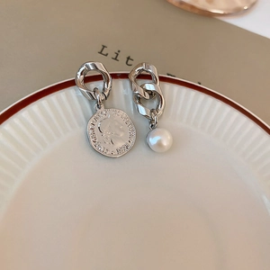 Detail of silver coin and pearl asymmetric earrings on a white ceramic plate