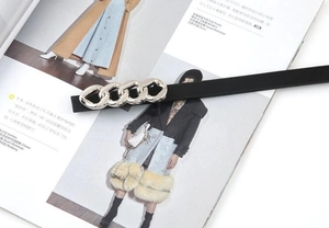 Detail of slim black leather belt with silver chain link buckle on a fashion magazine