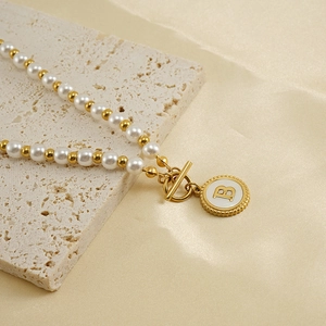 Detail of 18K gold-plated necklace with white pearls and initial B pendant on stone