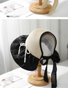 Close-up of straw sun hat featuring a black satin bow and elegant pearl embellishment