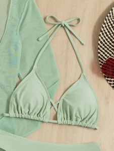 Close-up of light green bikini set with mesh cover-up and straw hat on wood background