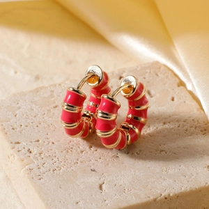 Macro detail of red enamel earrings with gold-tone striped accents on stone base