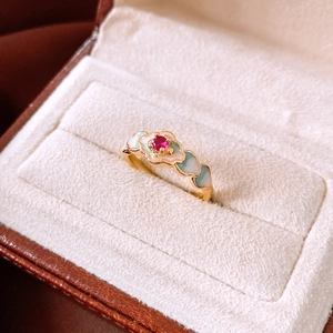 Close-up of 18K gold plated ring featuring a red gemstone and blue enamel cloud patterns
