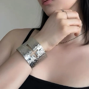 Macro shot of silver metal arm cuff with cross cutout detail on a female model