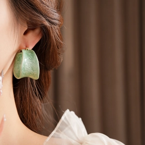 Detail of a light green marbled resin hoop earring worn by a model in a French retro style
