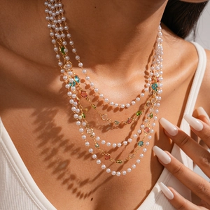 Detail of layered gold chain necklace featuring colorful gemstones and white faux pearls