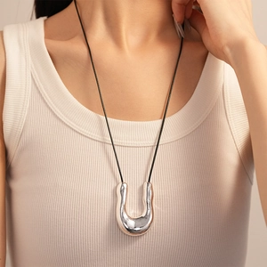 Model wearing a long silver U-shaped geometric pendant necklace with a black rope cord