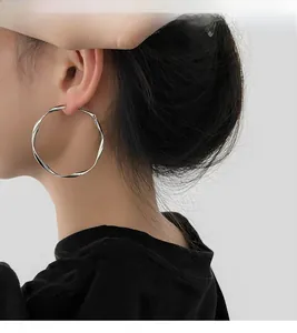 Close-up of a model wearing large silver twisted geometric hoop earrings in a minimalist style