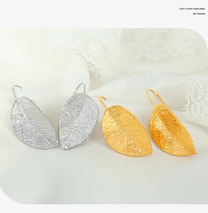 Detailed view of gold and silver leaf earrings on white lace fabric showing fine texture