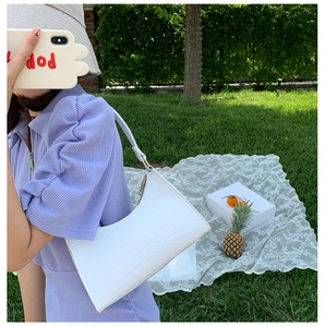 Detailed view of white crocodile pattern underarm bag on grass for summer picnic styling