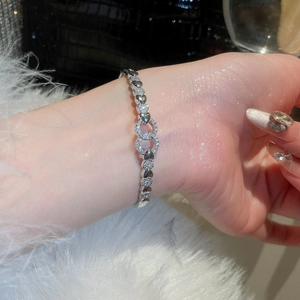 Detail of silver heart link bracelet featuring a crystal-encrusted geometric clasp on wrist