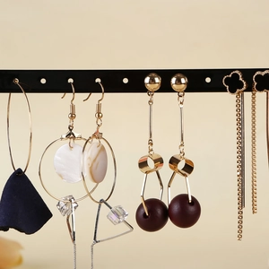 Side view of multi-style earrings on gold metal stand with solid beige background