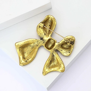 Macro detail of the golden bow brooch back showing the pin fastener and metal texture