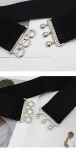 Detail of black elastic waist belt with silver metal three-hook buckle and woven texture