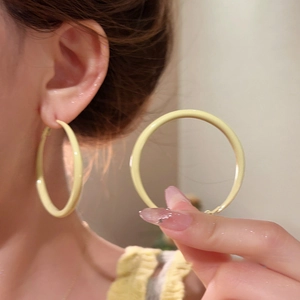 Close-up of a model wearing large pale yellow enamel hoop earrings with a soft finish