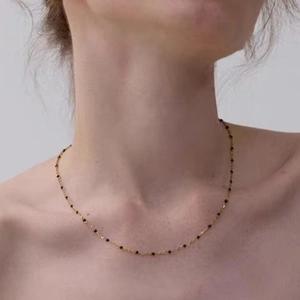 Minimalist gold chain necklace with black bead accents worn by a model in a close-up
