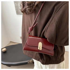 Close-up of vintage dark red glossy shoulder bag with gold metal clasp and knotted strap