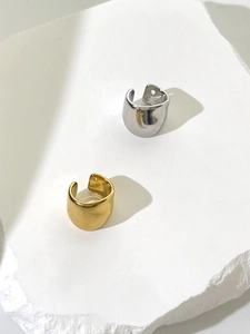 Detail view of wide-band gold and silver C-shape ear cuffs on a matte white stone