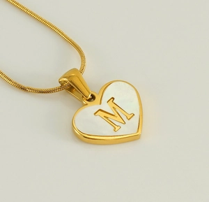 Macro shot of 18K gold plated heart pendant with M letter and white mother of pearl