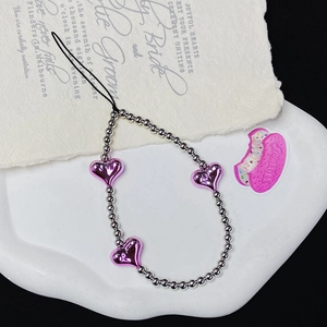 Detail of silver beads and pink hearts phone charm on a white decorative ceramic plate