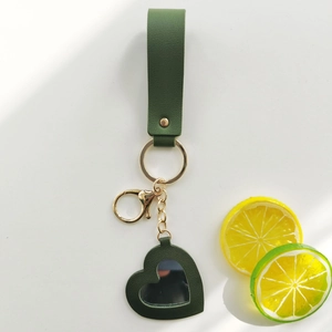 Detail view of dark green leather heart mirror keychain with gold hardware on white background