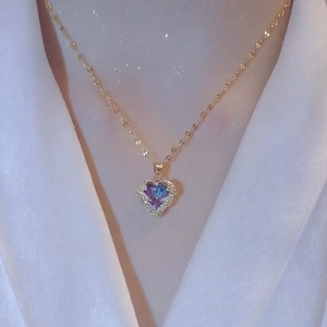 Golden heart necklace with gradient purple and blue stones on white silk background