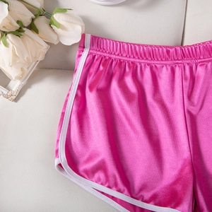 Detail of rose pink satin sports shorts with white contrast binding on a textured background
