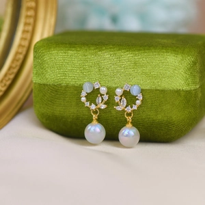 Detailed close-up of golden cat-eye earrings with pearls and zircons on green velvet