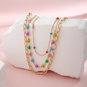 Detail of layered gold chains with colorful enamel heart charms on a stone display