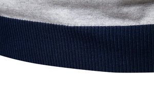 Detail eines grauen Strickpullovers mit dunkelblauem Rippsaum und Kontrastnähten