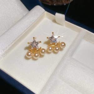 Detailed close-up of gold star pearl earrings with cubic zirconia in a velvet box