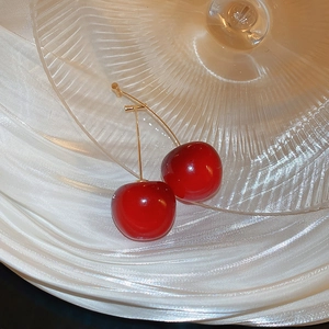 Vue macro des boucles d'oreilles cerises rouges brillantes avec tiges dorées sur verre