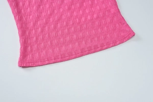 Détail de l'ourlet du gilet en tricot rose montrant la double couture et le tissu plissé