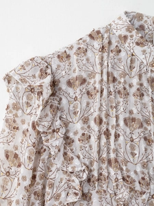 Gros plan sur tissu en mousseline blanche à fleurs brunes et détails volantés