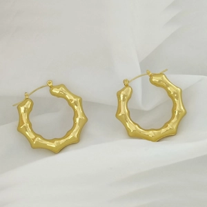 Close-up of golden U-shaped earrings with bamboo texture on white draped fabric