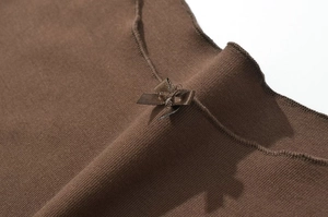 Close-up of brown ribbed knit dress featuring a delicate ribbon bow and ruffled neckline