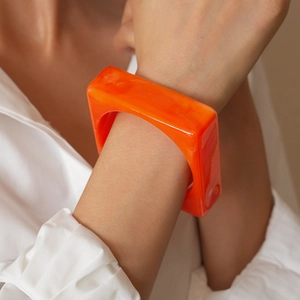 Close-up of vibrant orange square acrylic bangle showing resin texture and glossy finish