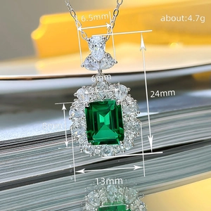 Macro shot of silver necklace featuring a large emerald cut green stone and diamond halo