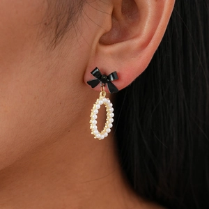 Macro view of a black bow earring with faux pearls and gold plating worn by a model
