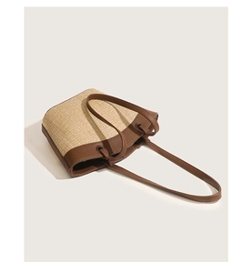 Close-up of woven straw handbag with brown leather trim and knotted strap detail
