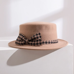 Détail rapproché d'un chapeau plat en laine camel avec nœud à motif pied-de-poule