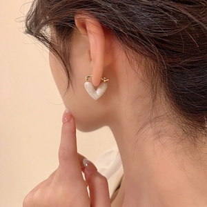 Close-up of heart-shaped pearl earrings in gold finish worn by a model in soft lighting