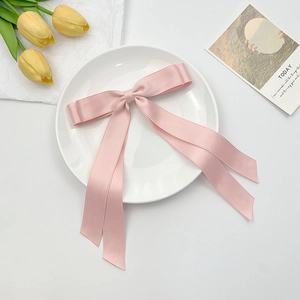 Detail of pink satin double-layer bow hair clip with long ribbons on white plate