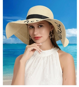 Detail of wide brim straw hat with Hello Sunshine embroidery on a sunny beach