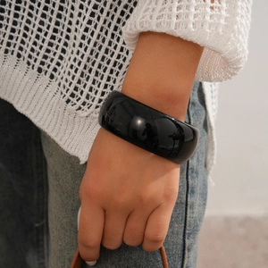Close-up of a wide glossy black resin geometric bangle worn on a woman's wrist
