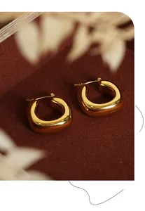 Polished gold U-shaped geometric hoop earrings on a dark red velvet background with dried flowers